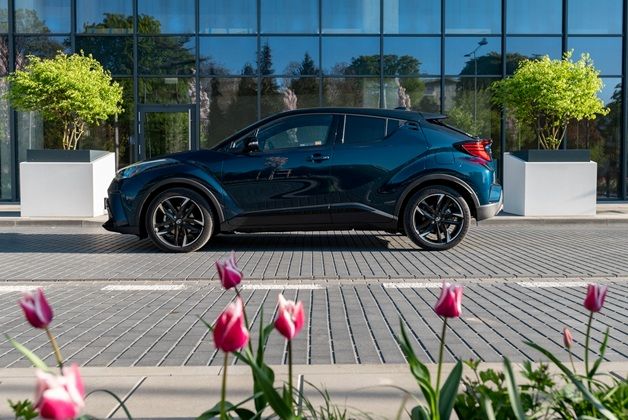 Ciemnoniebieska Toyota C-HR zaparkowana na tle szklanej fasady. Na pierwszym planie widoczne kwitnące biało różowe tulipany.