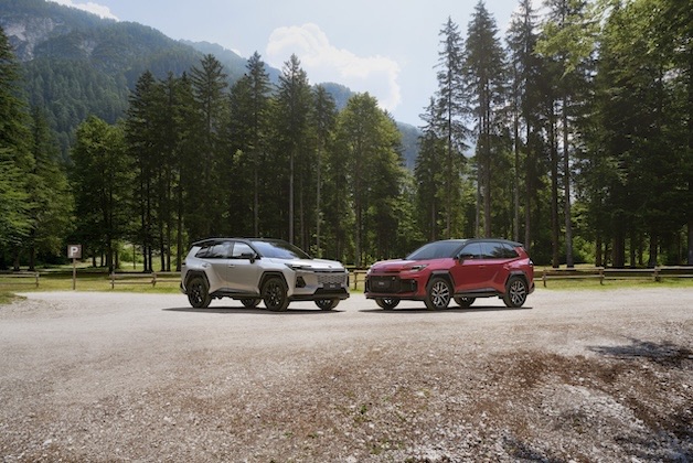 Srebrna elektryczna Toyota C-HR+ sfotografowana z profilu na tle nowoczesnego budynku mieszkalnego.