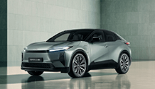 Na zdjęciu znajduje się samochód Toyota C-HR+ w kolorze srebrno-szarym, o nowoczesnej, aerodynamicznej sylwetce. Samochód jest zaparkowany w minimalistycznym, betonowym pomieszczeniu, co podkreśla jego futurystyczny design.
