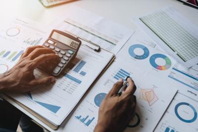 Ręce biznesmena lub księgowego używającego kalkulatora i długopisu do obliczania finansów, pracującego nad dokumentami z wykresami i danymi.