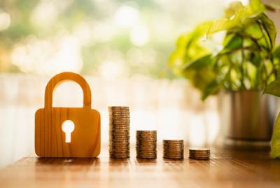 Drewniana kłódka obok rosnących stosów złotych monet, oświetlona jasnym, rozmytym tłem. Zdjęcie symbolizuje bezpieczeństwo finansowe, oszczędności, inwestycje i koncepcję bezpiecznego gromadzenia pieniędzy.