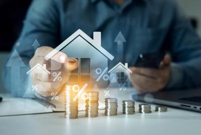 Zdjęcie przedstawia symboliczną wizualizację wzrostu stóp procentowych i cen nieruchomości z ikonami domów i stosami monet.