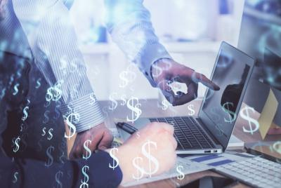 Biznesmen pracujący przy laptopie, przedstawiony w technice podwójnej ekspozycji z nałożonymi cyfrowymi symbolami dolara i wykresami giełdowymi.