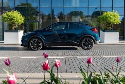 Ciemnoniebieska Toyota C-HR zaparkowana na tle szklanej fasady. Na pierwszym planie widoczne kwitnące biało różowe tulipany.
