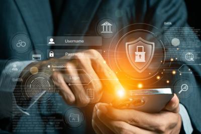 Grafika przedstawiająca dłonie osoby trzymającej smartfona, na który nałożone są cyfrowe ikony bezpieczeństwa. W centralnym punkcie widoczna jest świecąca tarcza z symbolem kłódki, pola logowania „Username” i „Password” oraz ikony odcisku palca i budynku banku, co symbolizuje bezpieczną bankowość mobilną i ochronę danych.