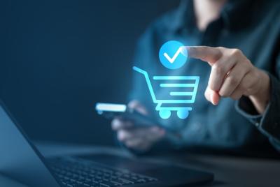 Mężczyzna dokonujący zakupu online za pomocą smartfona i laptopa – widoczna jest niebieska ikona koszyka.
