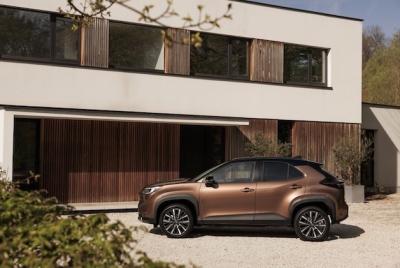 Brązowy SUV Toyota Yaris Cross zaparkowany przed nowoczesnym, białym domem z drewnianą elewacją.