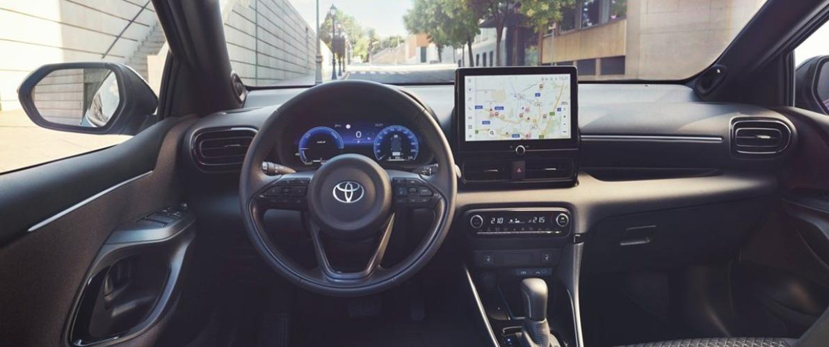 Wnętrze nowej Toyoty Yaris Hybrid z widokiem na deskę rozdzielczą, kierownicę i ekran multimedialny.