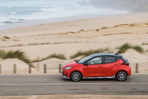 Czerwona Toyota jadąca drogą obok pustynnych terenów, widoczne rosnące kępy trawy