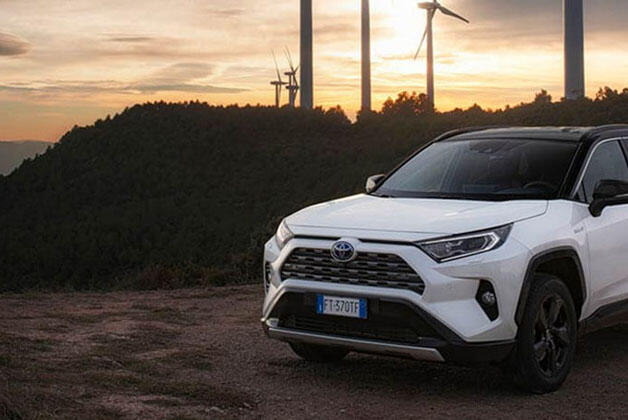 Biała Toyota stojąca na tle wzgórz, w tyle widoczne wiatraki