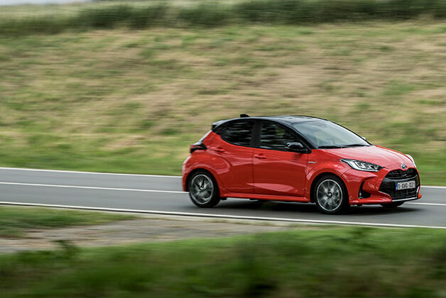 Czerwona Toyota Yaris, jadąca drogą pośród zielonych łąk