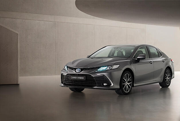 Szara Toyota Camry Hybrid, stojąca na szarym, betonowym podłożu, w tle betonowe ściany, u góry szary, podwieszany, półokrągły sufit