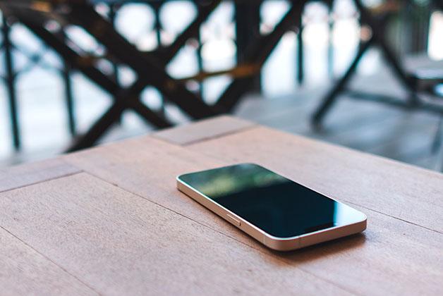 Na zdjęciu widać leżący na drewnianym stole telefon. Tło zdjęcia jest rozmyte.