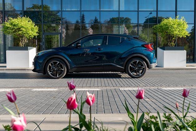 Ciemnoniebieska Toyota C-HR zaparkowana na tle szklanej fasady. Na pierwszym planie widoczne kwitnące biało różowe tulipany.