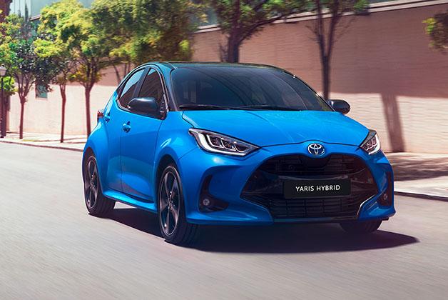 Niebieska Toyota Yaris Hybrid jadąca miejską ulicą w słoneczny dzień.
