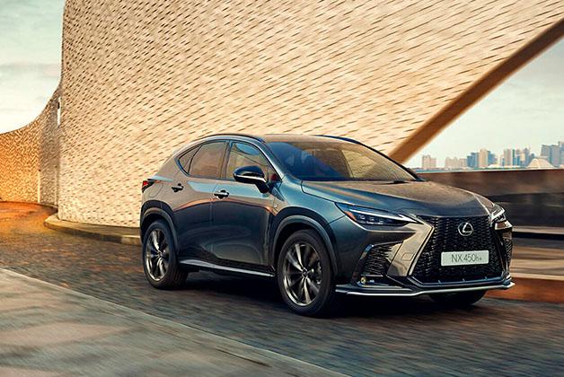 Lexus NX 450h+ w kolorze grafitowym jadący drogą na tle nowoczesnej architektury.