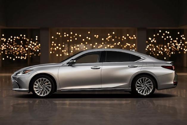 Srebrny luksusowy sedan Lexus ES pokazany z boku, zaparkowany w ciemnym pomieszczeniu z rozmazanymi, ciepłymi lampkami w tle.