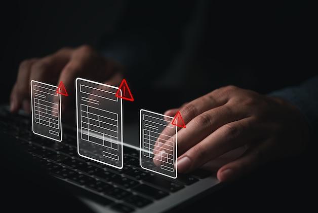 Dłonie piszące na laptopie i cyfrowe ikony dokumentów z czerwonymi znakami ostrzegawczymi.