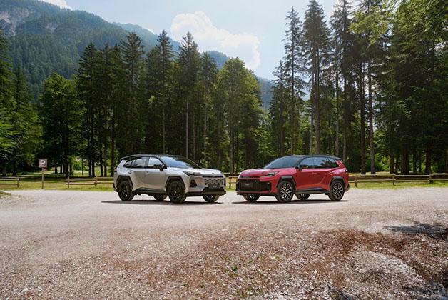 Dwa SUV-y Toyota RAV4 szóstej generacji, biały i czerwony, zaparkowane na leśnej polanie na tle gór.